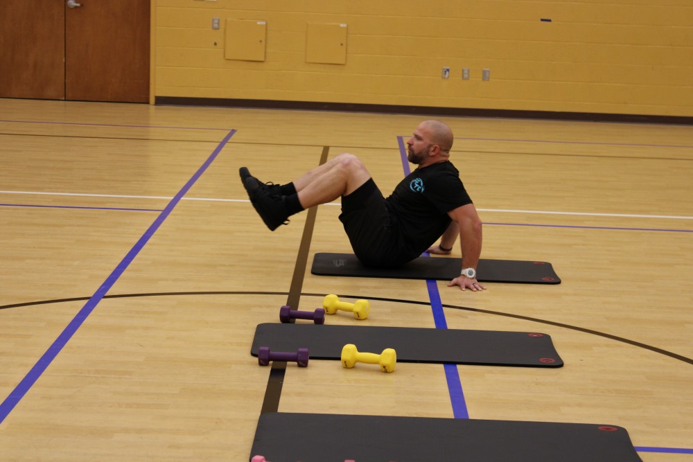 One man stretching on a yoga mat on the ground with weights on the floor next to him